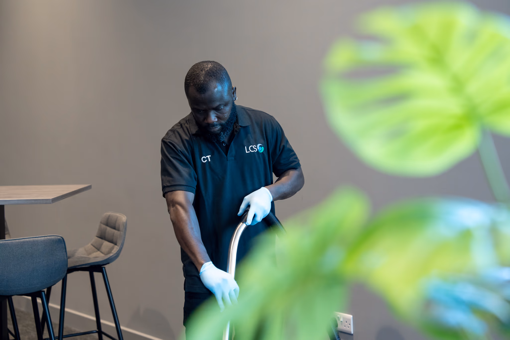 LCS male member of staff hoovering with green foliage in foreground