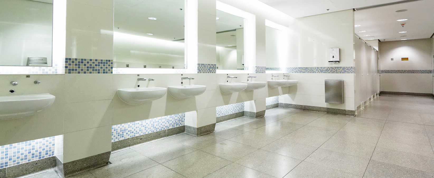 big public bathroom with sinks and cubicles visible with light walls and flooring
